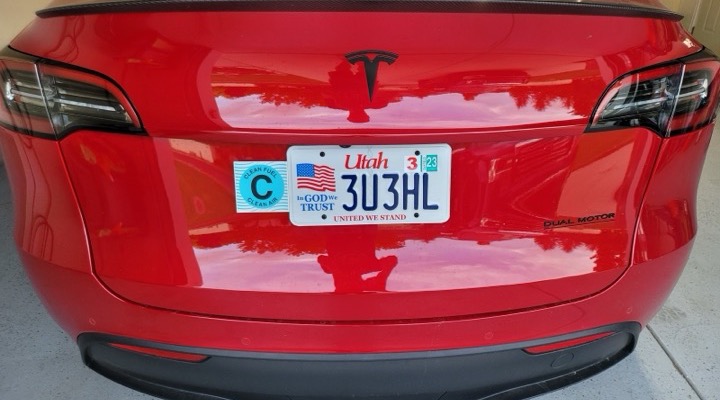 The back of a red Tesla with a Clean Fuel sticker on an aluminum bracket beside the Utah license plate